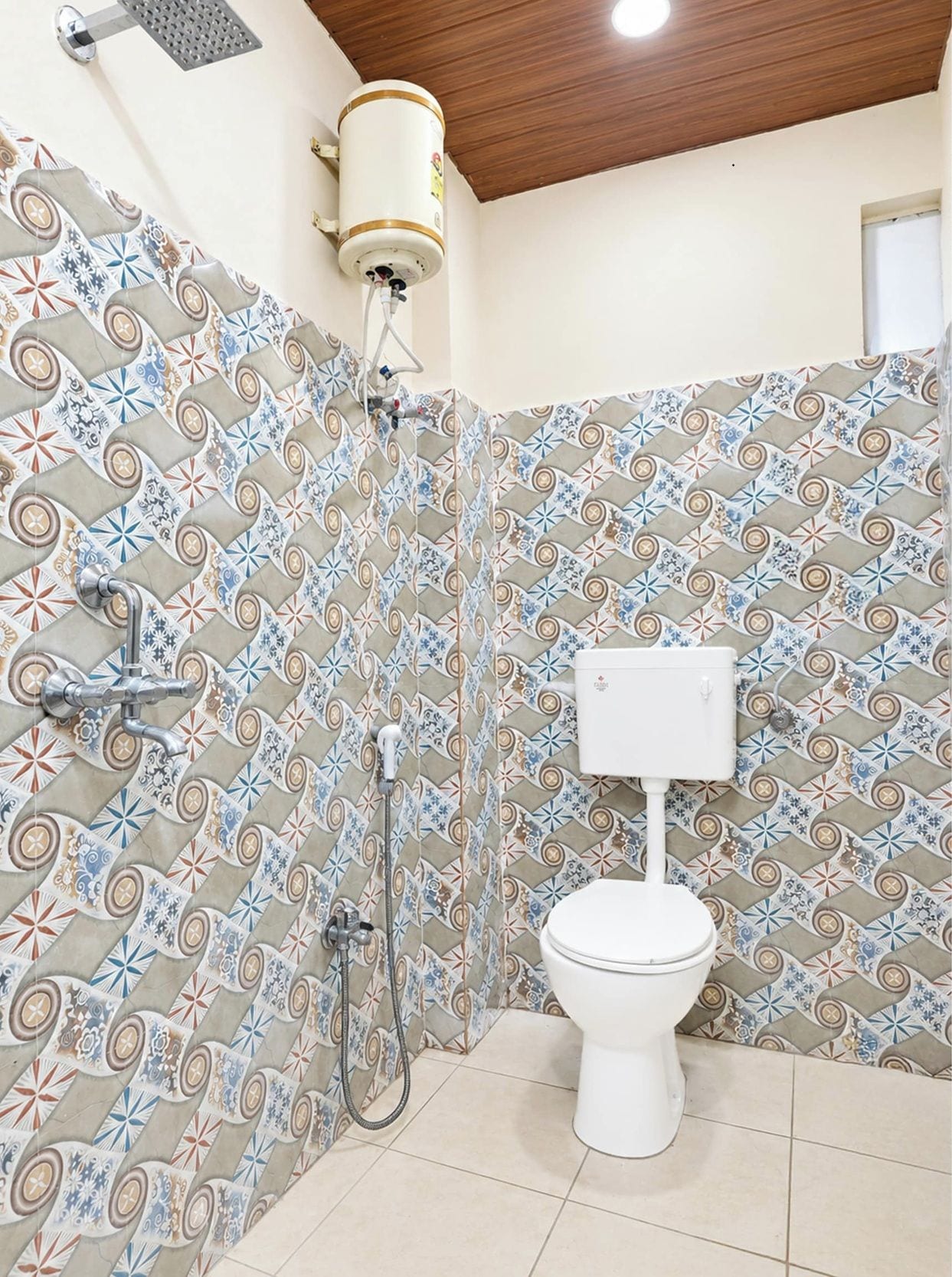 Casa de banho com painel de azulejos estampados, sanita branca, chuveiro com chuveiro manual e termoacumulador fixado na parede.