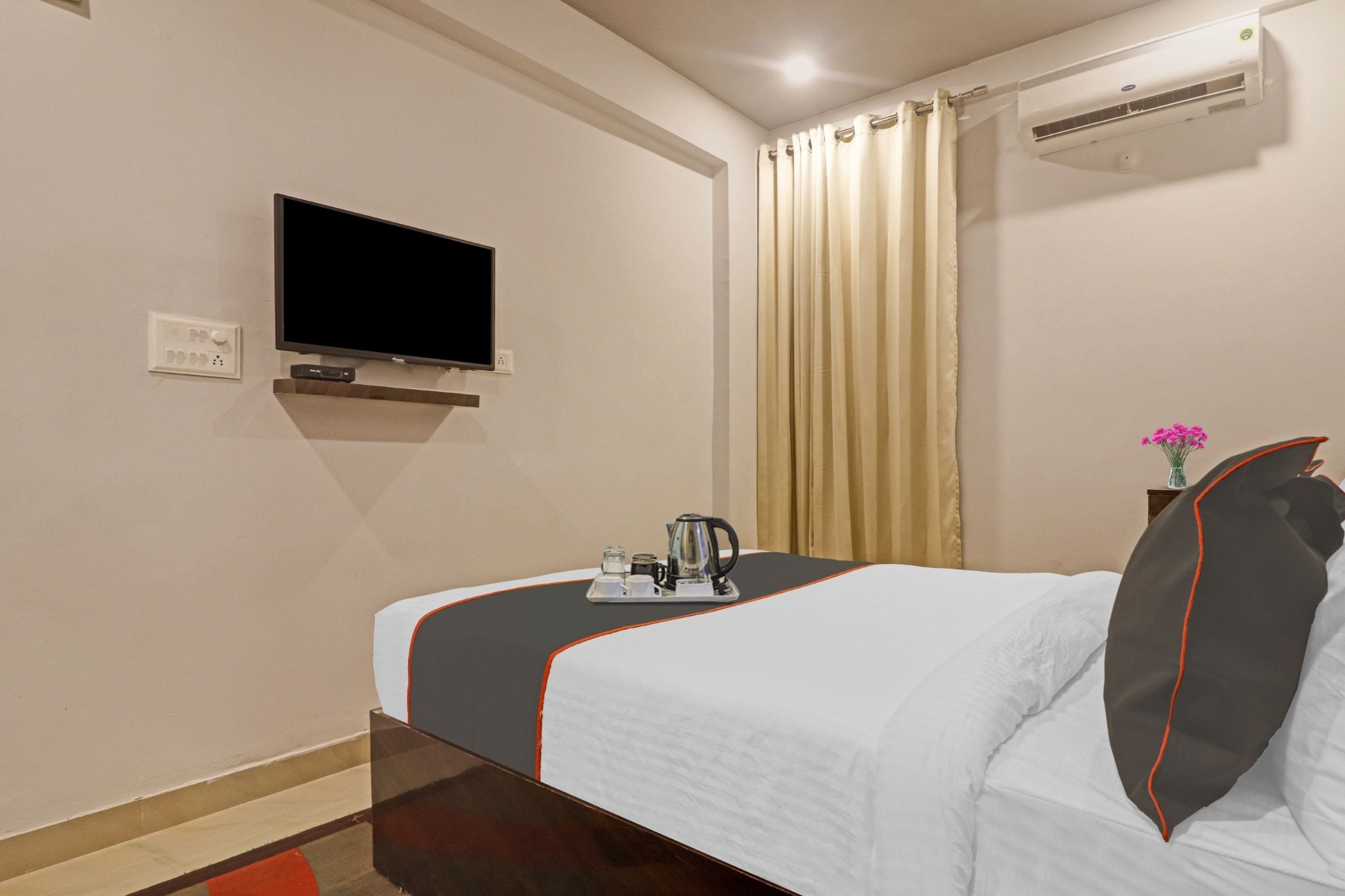 Quarto de hotel com cama, televisão na parede, janela com cortinas e ar condicionado.