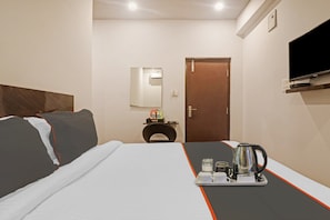 A hotel room with a bed, a bedside table with a lamp, a TV mounted on the wall, and a tray with a coffee pot and cups. - Super Townhouse RCC Pristine (Hyderabad)