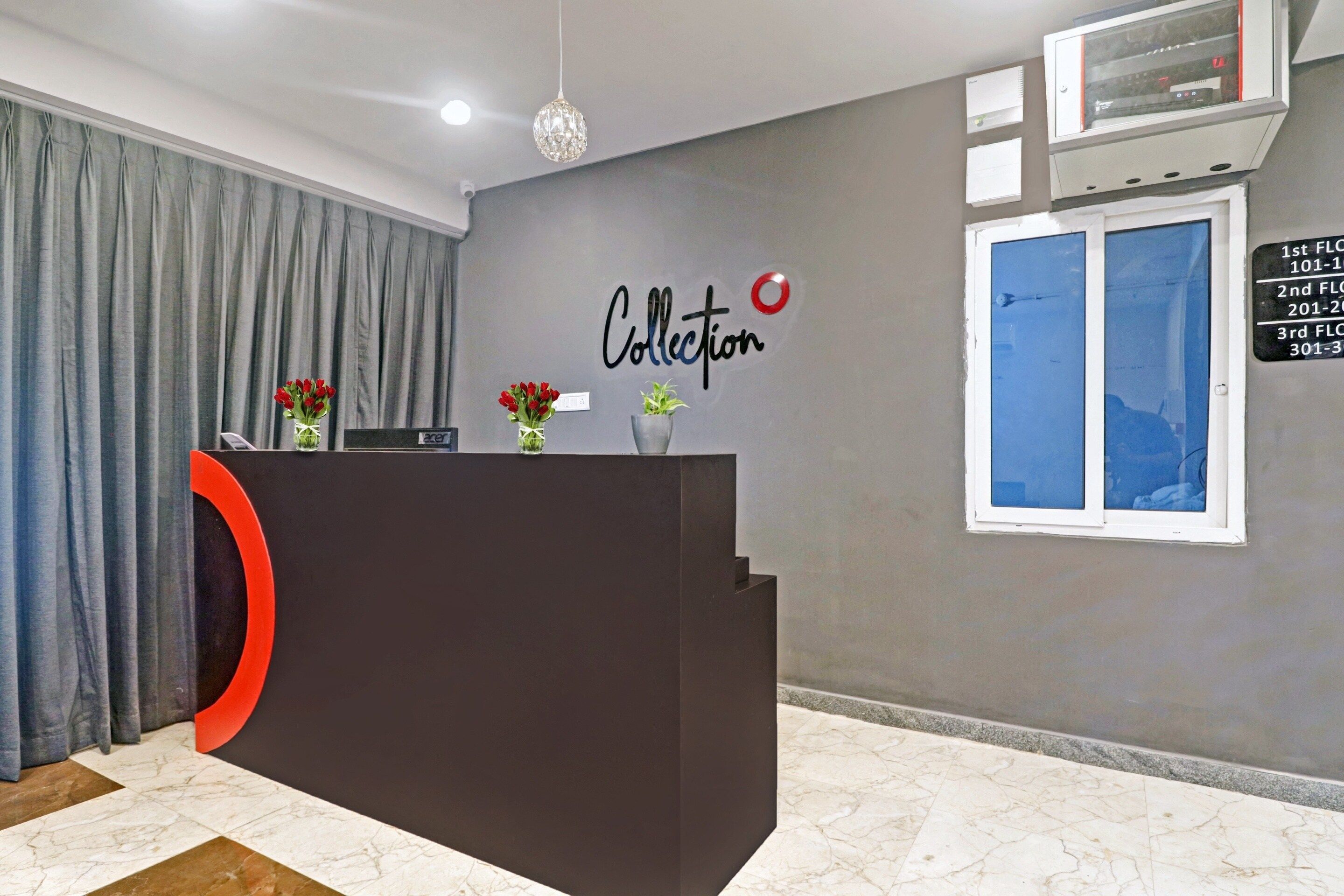 Bancada de recepção com design moderno, parede cinza com a inscrição 'Collection', janela com informações de contato e uma cortina.