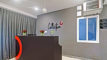 Bancada de recepção com design moderno, parede cinza com a inscrição 'Collection', janela com informações de contato e uma cortina.
