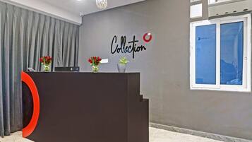 Bancada de recepção com placa, parede com sinalização indicando 'Collection' e janela com persianas.