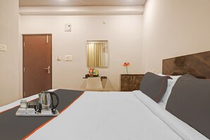 A hotel room with a bed, a bedside table with a kettle and a tray, a small table with snacks, a mirror, and a door. - Super Townhouse RCC Pristine (Hyderabad)
