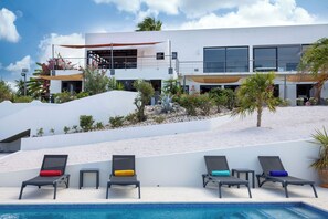 A modern building with a pool area featuring multiple lounge chairs and a clear blue pool. - Casa Pasha - Apartment Tiara - Jan Thiel (Jan Thiel)
