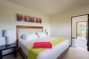 A hotel room with a bed, two bedside lamps, a painting of flowers on the wall, and a view of the outside. - Casa Pasha - Apartment Tiara - Jan Thiel (Jan Thiel)