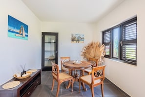 Uma sala de jantar com uma mesa de madeira redonda, quatro cadeiras e uma porta de vidro que dá para a cozinha.