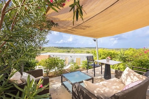 An outdoor patio with wicker furniture, a table, and a view of a hilly landscape. - Casa Pasha - Apartment Tiara - Jan Thiel (Jan Thiel)
