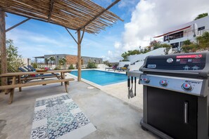 Ein Grill mit Bedienelementen, ein Pool, Liegestühle und eine Pergola.