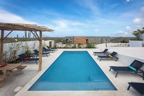 A rectangular swimming pool with lounge chairs and a pergola on a rooftop terrace. - Casa Pasha - Apartment Tiara - Jan Thiel (Jan Thiel)