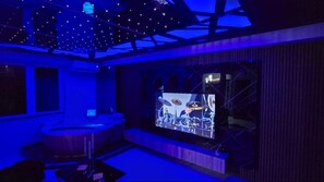 A room with a large screen displaying a band performance, a bar area, and a ceiling with a geometric light fixture. - Scenic Luxury 1-BR Apartment with King Bed & Private Jacuzzi in Vodno, Skopje (Скопје)