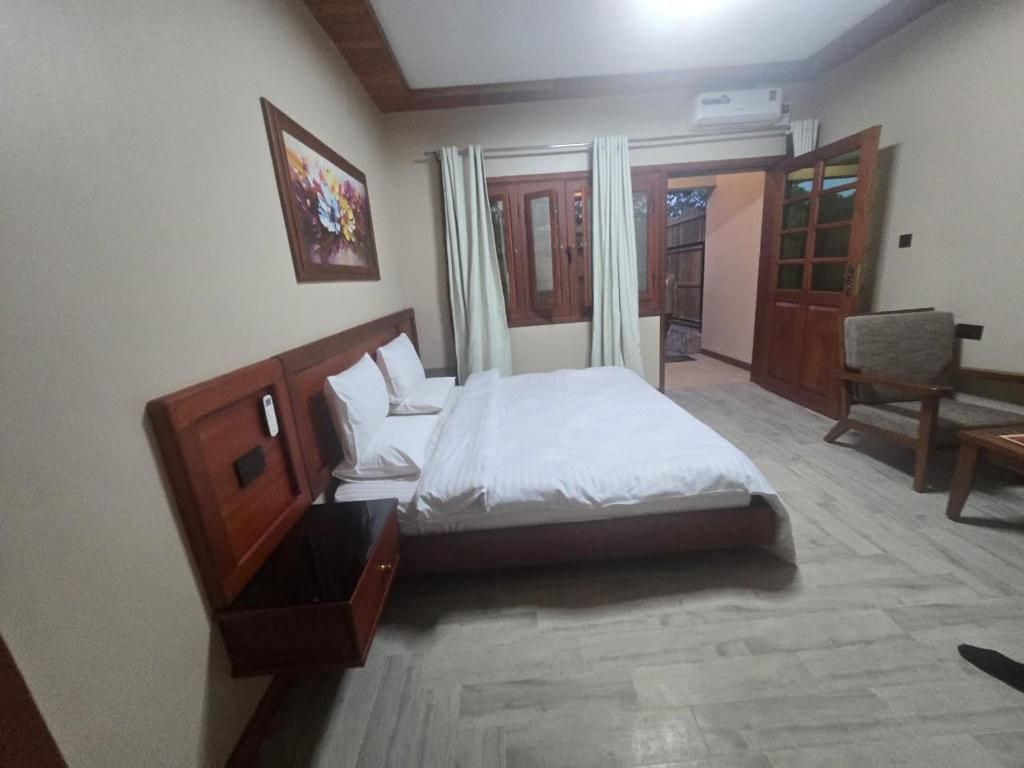 Quarto de hotel com uma cama, uma cadeira, um armário de madeira, um quadro na parede e uma porta que dá para uma varanda.