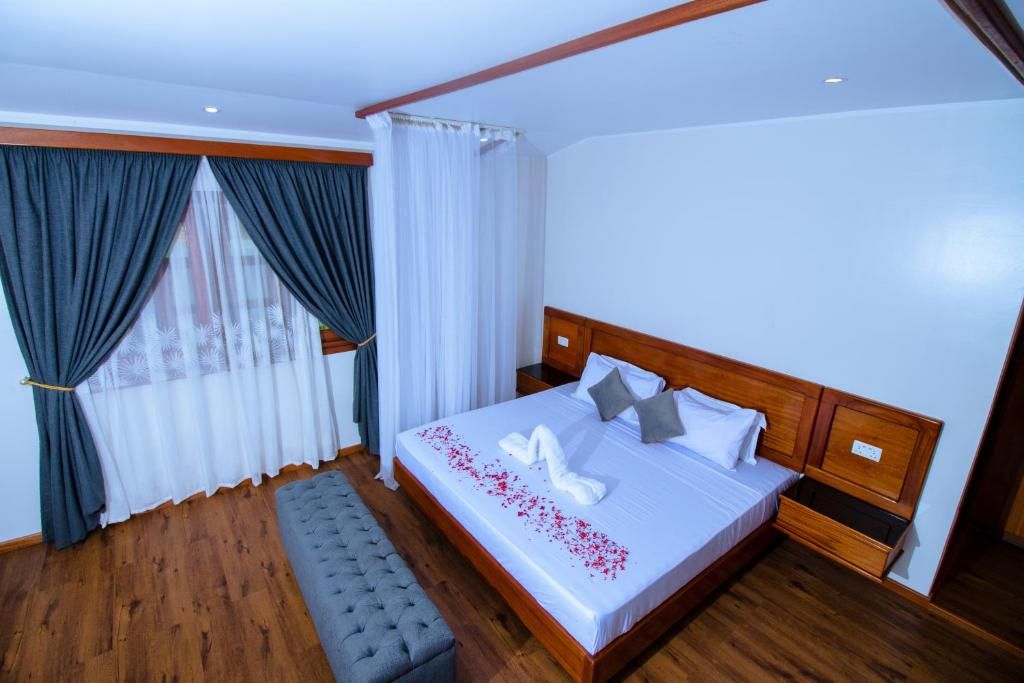 A neatly made bed with pillows and a decorative swan on the bedspread, a wooden headboard, a bench, and a window with curtains.