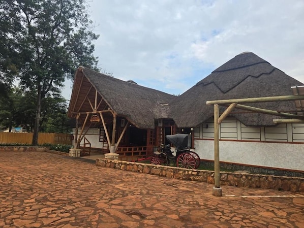 A traditional thatched-roof building with a wooden structure, a stone-paved courtyard, and a horse-drawn carriage. - Across the Nile Resort Jinja (Jinja)