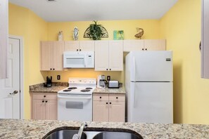 A compact kitchen with a microwave, stove, and refrigerator, featuring light wooden cabinets and a granite countertop. - Close To Disney Condo 3 Bed / 2 Bath 3 Bedroom Condo (Kissimmee)