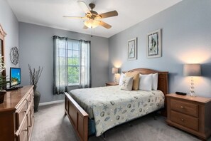 Un dormitorio con cama, mesitas de noche, ventilador de techo, ventana con cortinas y decoración en la pared.