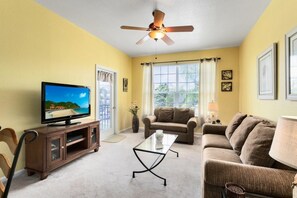 Una sala de estar con televisor, ventilador de techo, sofá y mesa de centro.