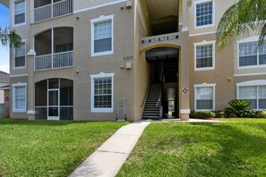 Un edificio residencial de varios pisos con entrada despejada, un cartel de dirección visible y una escalera que conduce a la entrada.