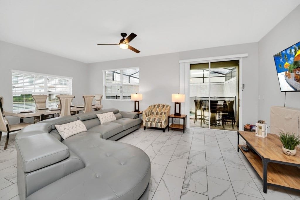 A spacious living room with a large sectional sofa, a dining area with a glass door, and a ceiling fan.