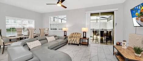 A spacious living room with a large sectional sofa, a dining area with a glass door, and a ceiling fan.