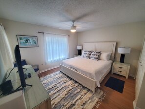 Ein Schlafzimmer mit einem Bett, Nachttischen, einem Schreibtisch, einem Deckenventilator und einem Fenster mit Jalousien.