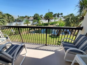 A balcony with two white wicker chairs and a small table, overlooking a pool and greenery. - Ocean Village Club I25 2 Bedroom Condo (St. Augustine)