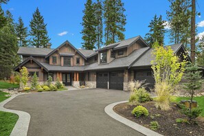 A large, multi-story log cabin with a stone foundation, a curved driveway, and a well-maintained front yard with various shrubs and trees. - Private Pool! Stunning View Overlooking Hole #4 on the Rope Rider Golf Course (Cle Elum)