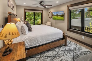 A bedroom with a large bed, a ceiling fan, a view of a golf course, and a window with a view of trees. - Private Pool! Stunning View Overlooking Hole #4 on the Rope Rider Golf Course (Cle Elum)