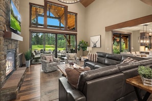 A spacious living area with a fireplace, leather sofa, and a large window overlooking a golf course. - Private Pool! Stunning View Overlooking Hole #4 on the Rope Rider Golf Course (Cle Elum)