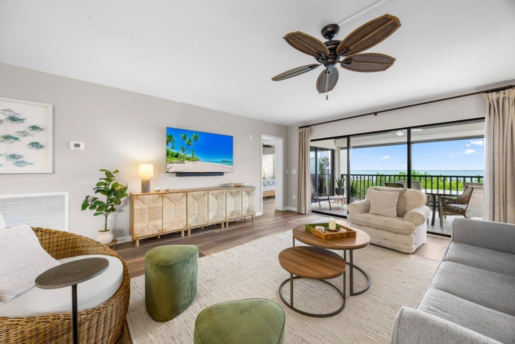 A modern living room with a large window, a ceiling fan, and a view of the ocean.