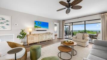 A modern living room with a large window, a ceiling fan, and a view of the ocean.