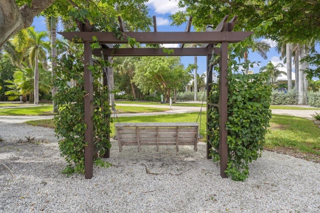 A wooden pergola with a bench underneath, surrounded by gravel and greenery.