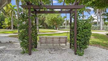 A wooden pergola with a bench underneath, surrounded by gravel and greenery.