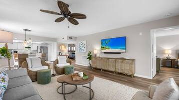 A modern living room with a ceiling fan, a flat-screen TV, and a dining area.
