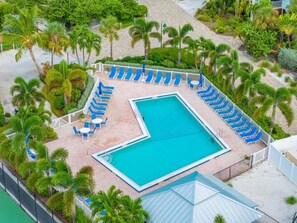 A pool area with a rectangular pool, surrounded by blue lounge chairs and palm trees. - Sunset Captiva Bayside Unit 104-new 2 Bedroom Condo (Captiva)