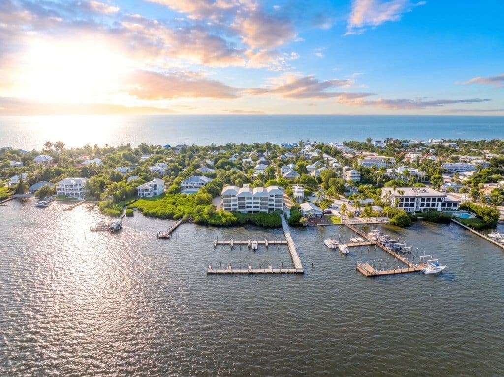 An aerial view of a coastal town with a marina, residential buildings, and a large hotel with a modern design.