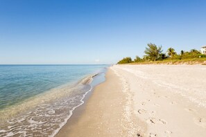 Ein Strand mit klarem Wasser, sandigem Ufer und einem Gebäude mit weißem Dach.