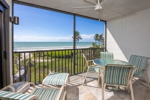 A balcony with a view of the beach, a table with chairs, and a ceiling fan. - Pelicans Roost 303 2 Bedroom Condo (Sanibel)