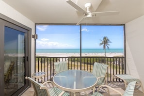 A balcony with a glass table and chairs, overlooking a beach with palm trees and the ocean. - Pelicans Roost 303 2 Bedroom Condo (Sanibel)