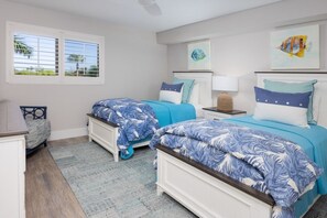 A bedroom with two beds, a window with blinds, a nightstand, and artwork on the wall. - Pelicans Roost 303 2 Bedroom Condo (Sanibel)