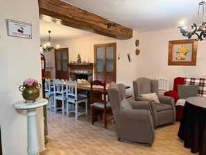 Ein gemütliches Wohnzimmer mit Kamin, ein Essbereich mit Holztisch und Stühlen sowie eine Sitzecke mit Sesseln und einer Couch.
