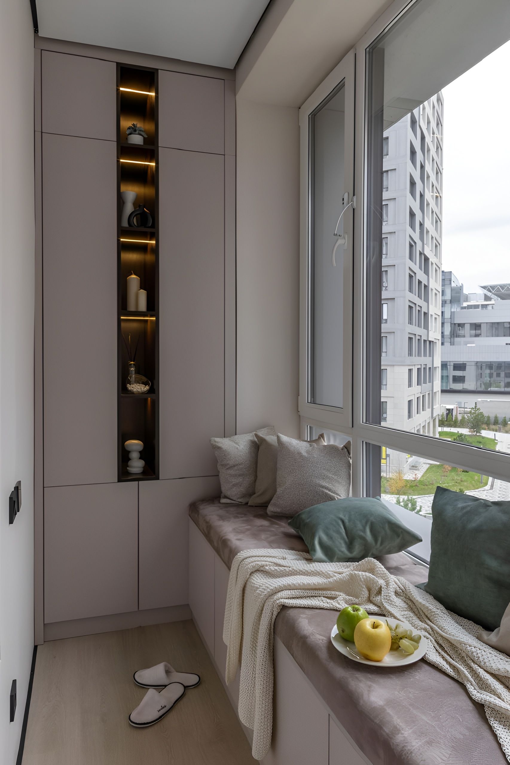 Ein kleiner Balkon mit einer eingebauten Ablage, einer Sitzecke mit Kissen und Blick auf die Stadtlandschaft.