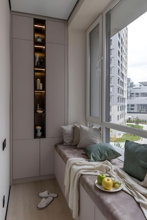 Ein kleiner Balkon mit einer eingebauten Ablage, einer Sitzecke mit Kissen und Blick auf die Stadtlandschaft.