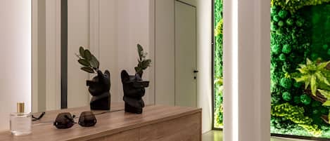 A modern bathroom with a wooden vanity, a green textured bench, and a green wall with a plant display.