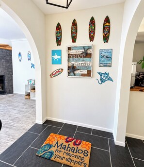 A hallway with surfboards, a surf-themed sign, and a welcome mat.