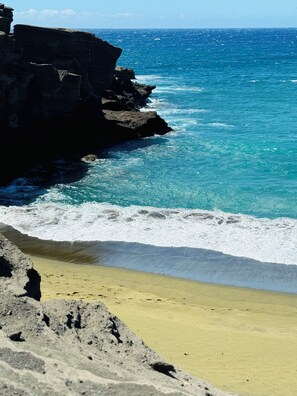 A coastal landscape with a rocky cliff and a sandy beach.