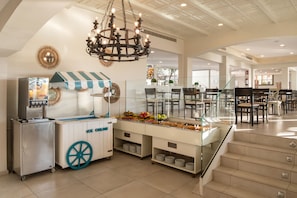 A modern kitchen area with a food service station, a chandelier, and a seating area with tables and chairs. - Hotiday Fuerteventura Seafront (Antigua)