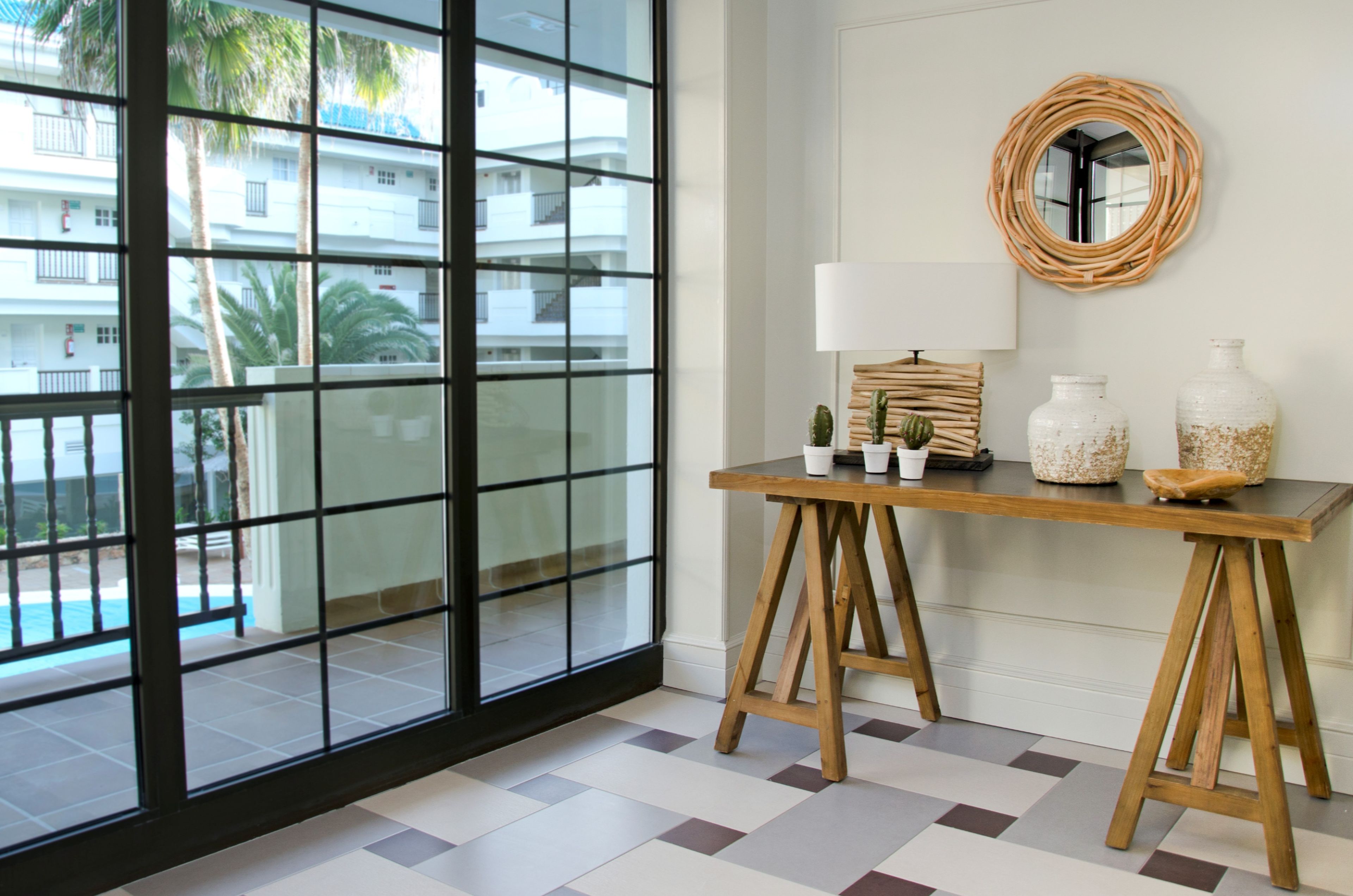 Una habitación con un ventanal grande, una mesa de madera con una lámpara y objetos decorativos.