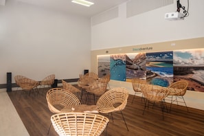 A room with wicker chairs, a projector, and a wall with 'Erezadventure' text and images. - Hotiday Fuerteventura Seafront (Antigua)