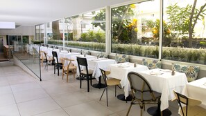 Un restaurante con mesas y sillas dispuestas a lo largo de una pared de vidrio, con vistas a un jardín.