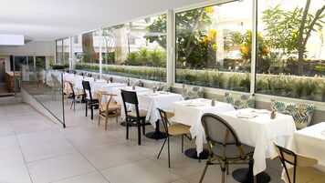 Un restaurante con mesas y sillas dispuestas a lo largo de una pared de vidrio, con vistas a un jardín.